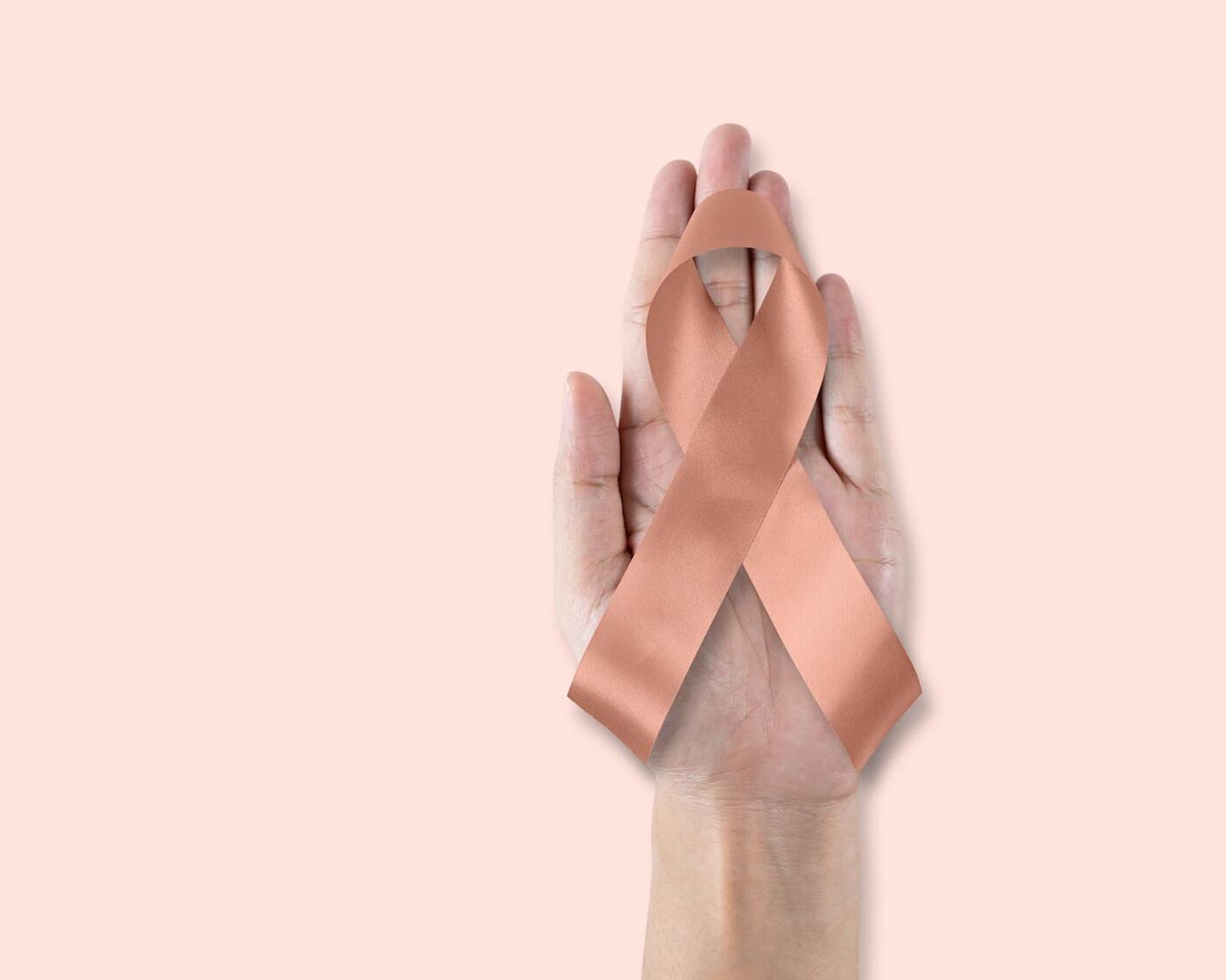 Hand hält eine rosafarbene Schleife als Symbol für Brustkrebs.